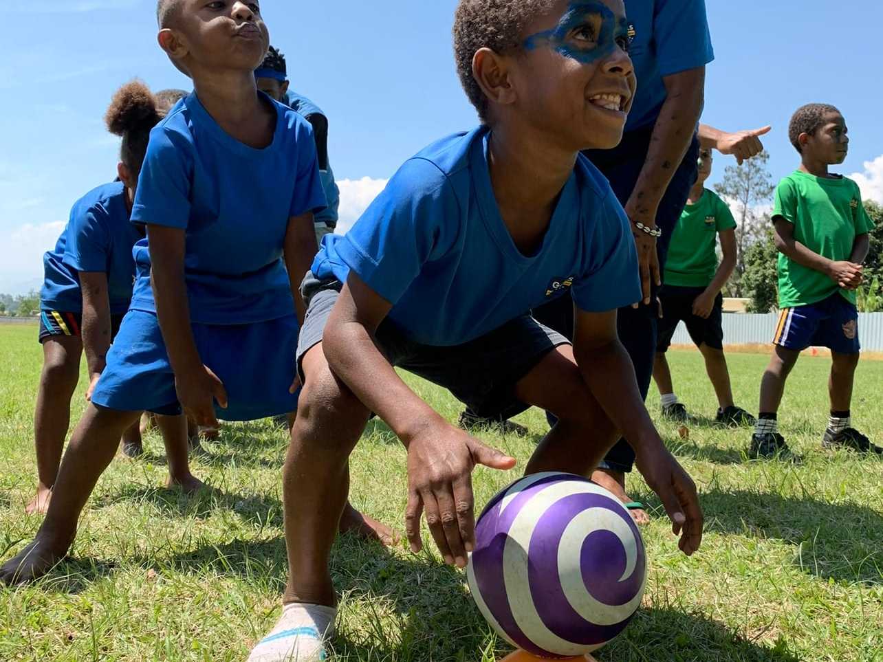 Young students in blue uniforms playing ball games on the school field.