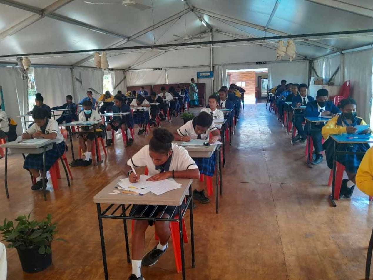 Secondary students sitting an examination in a large hall.