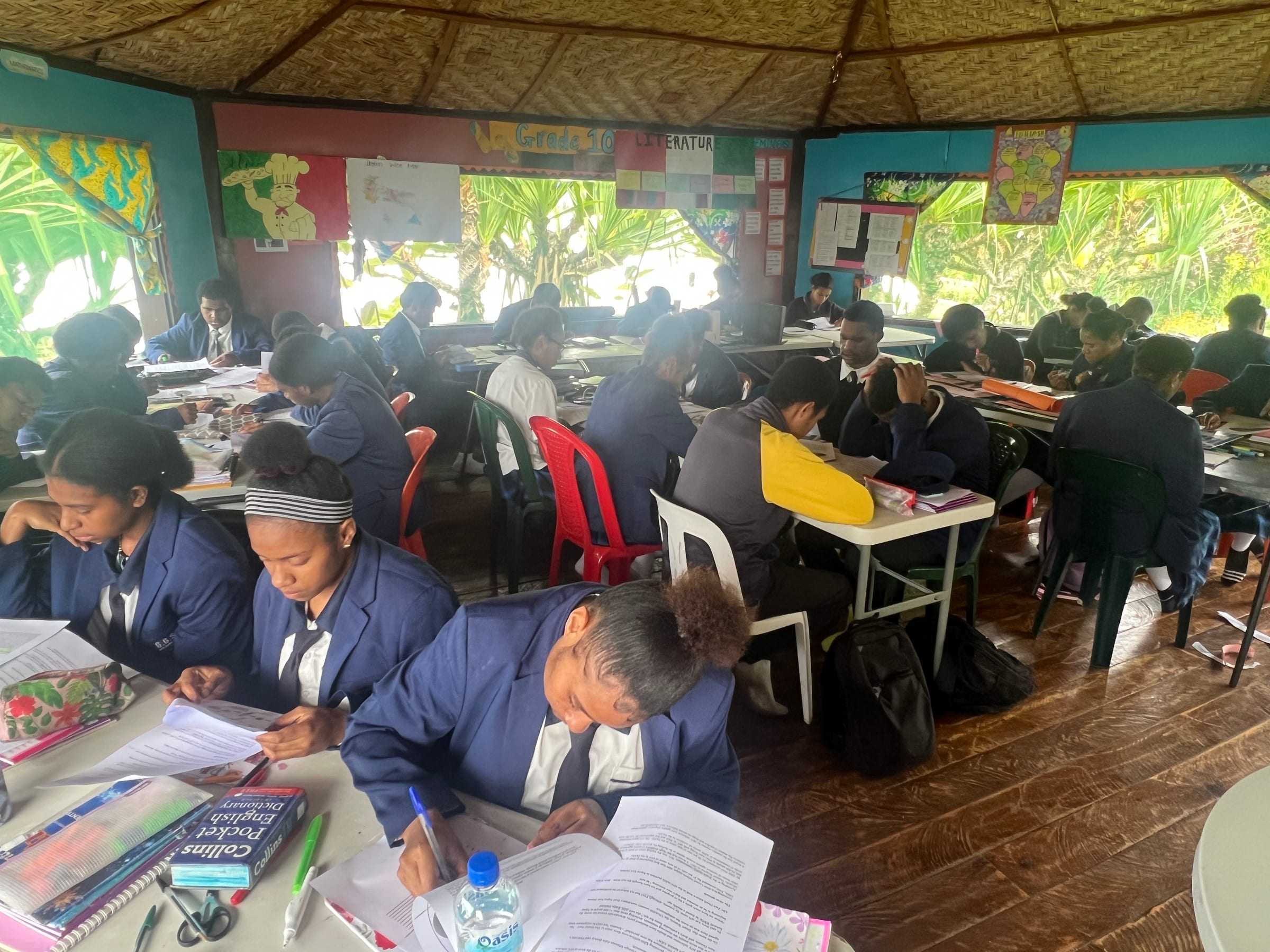 Secondary students in navy blazers working at their desks in an open-sided classroom.